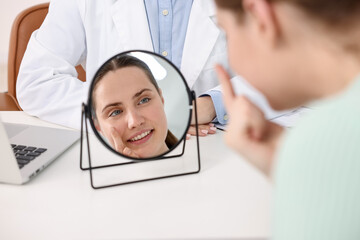 Young woman putting on contact lenses at table near mirror in ophthalmologist office, selective...