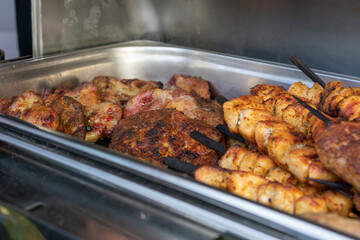 Variety of meat are grilled and served on skewers. The skewers are arranged in a metal tray, and...