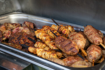 Variety of meat are grilled and served on skewers. The skewers are arranged in a metal tray, and...