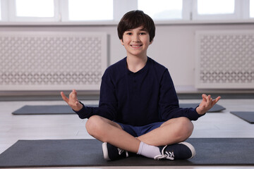 Happy boy practicing yoga on mat indoors