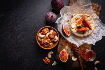 Brie cheese on a wooden Board with fresh figs and honey over dark table, top view