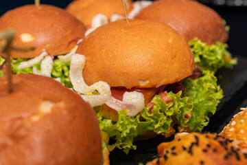 Close-up of gourmet mini burgers with fresh lettuce, pulled pork, crispy toppings, and golden buns...