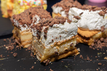 Dessert with chocolate chips and whipped cream on top. The dessert is cut into four pieces. The dessert is on a black surface.
