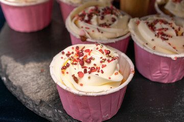 Row of cupcakes with pink paper cups and red sprinkles on top. The cupcakes are arranged on a black surface.