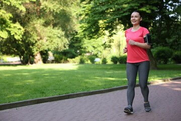Sporty woman with armband running in park, space for text