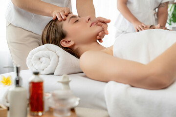 Caucasian couple enjoying relaxing anti-stress head massage and pampering facial beauty skin recreation leisure in dayspa modern light ambient at luxury resort or hotel spa salon. Quiescent