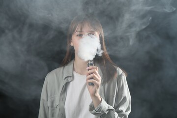 Woman using electronic smoking device on dark background