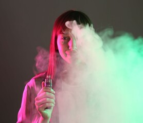Woman using electronic smoking device in neon lights on grey background