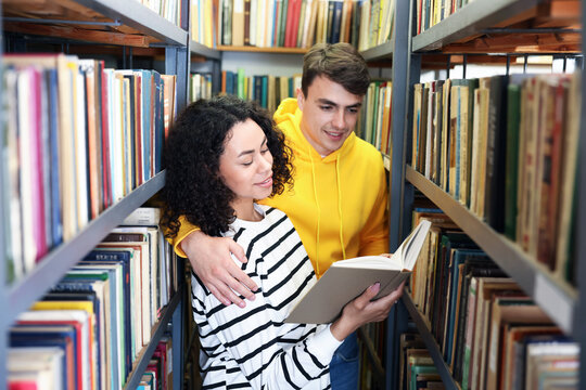 Students studying together near shelves with books in public library