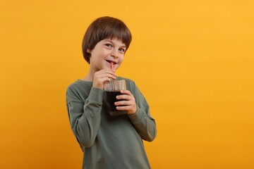 Cute little boy drinking refreshing soda on orange background