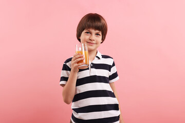 Cute little boy with glass of orange juice on pink background. Refreshing drink