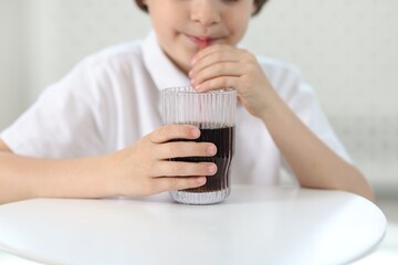 Little boy drinking refreshing soda at table indoors, closeup