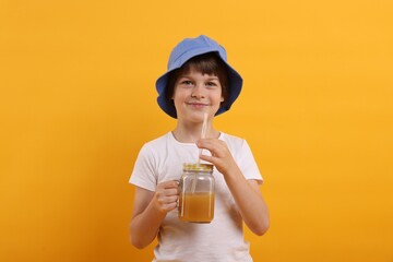 Cute little boy in panama hat with mason jar of juice on orange background. Refreshing drink