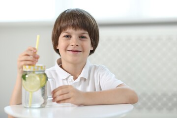 Cute little boy with mason jar of lemonade at table indoors. Refreshing drink