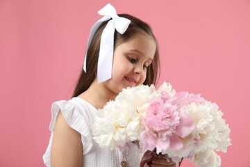 Cute little girl with bouquet of beautiful peonies on pink background