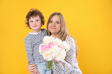 Little boy giving his mom beautiful peony flowers on yellow background