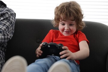 Little boy and his father playing with game controller together at home