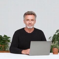 Financial planning retirement tools concept. A man with gray hair sits at a table with a laptop, surrounded by indoor plants.