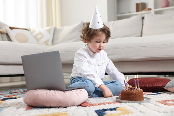 Birthday celebration. Little boy with cake having video call via laptop at home