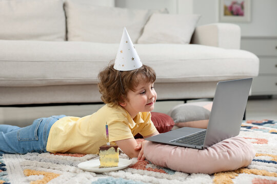 Birthday celebration. Little boy with piece of cake having video call via laptop at home