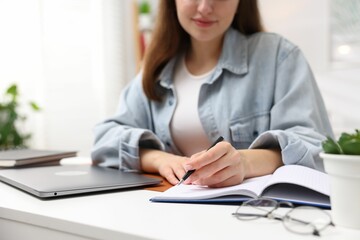 Woman with planner and laptop at white desk indoors, closeup