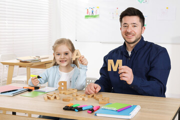 Little girl learning letters with teacher at desk indoors