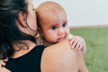 Baby girl holding mother's shoulder while looking away