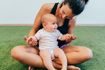 Mother holding baby while sitting on green carpet: motherhood and childcare concept