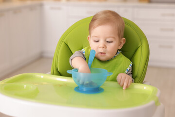 Cute little baby eating healthy food in high chair indoors
