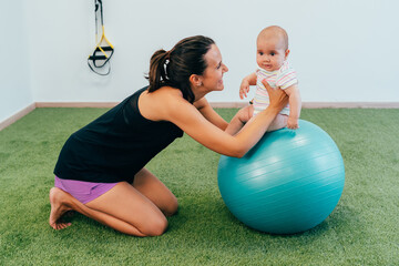 Physiotherapist helping baby doing exercises on fitness ball