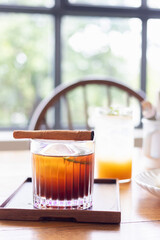 An Americano over a single sphere of ice, crowned with a cinnamon stick softly kissed by flame.