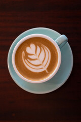 Cup of coffee with latte art on wooden table with soft sunlight. Top view