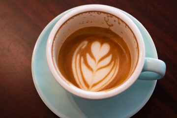 Cup of coffee with latte art on wooden table with soft sunlight. Perfect latte art on the bottom of cup.
