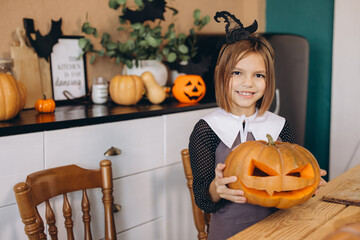 Smiling girl holding carved pumpkin celebrating Halloween at home