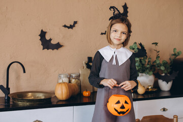 Little Girl Wearing Witch Costume Holding Pumpkin Basket Celebrating Halloween in Kitchen