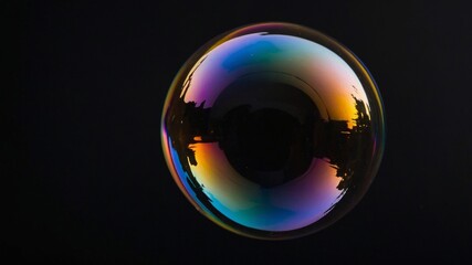 Colorful Soap Bubble Floating Against a Dark Background Reflecting Silhouettes and Hues in a Striking Display of Light