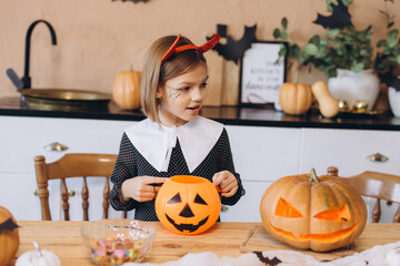 Little Girl Wearing Devil Costume Holding Jack o' lantern Celebrating Halloween at Home