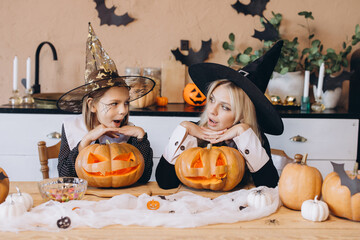 Mother and daughter wearing witch costumes looking at carved pumpkins for Halloween