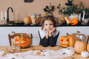 Little witch celebrating Halloween with carved pumpkins and candies