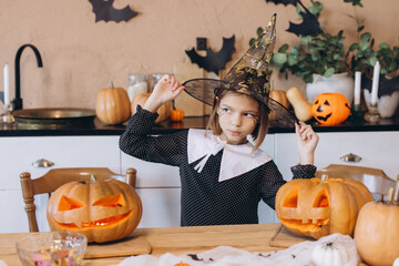 Little girl wearing witch hat celebrating Halloween with carved pumpkins