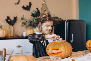 Little Girl Wearing Witch Costume Carving Halloween Pumpkin at Home