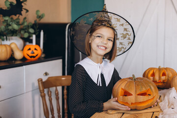 Smiling girl wearing witch costume holding carved pumpkin celebrating Halloween