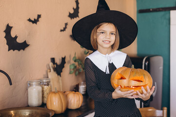 Little witch holding jack o' lantern celebrating Halloween in kitchen