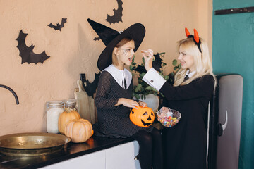 Mother and daughter wearing Halloween costumes eating candies in the kitchen