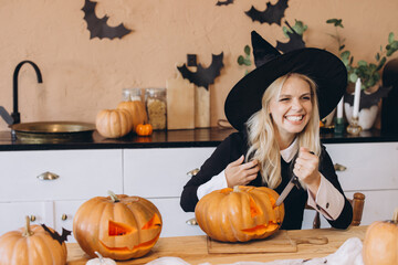 Woman wearing witch hat carving pumpkins for Halloween party