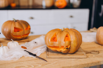 Carving smiling halloween pumpkins on kitchen table with knife and spider decorations