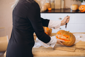 Woman carving a pumpkin for Halloween party in kitchen