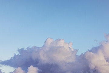Dark thunderclouds with purple tones rising high against evening blue sky before summer storm....