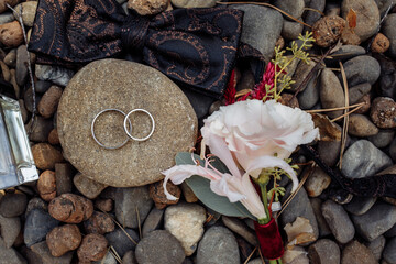 Three wedding rings placed on a smooth stone surrounded by natural pebbles, symbolizing unity,...