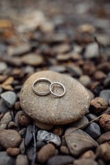 Three wedding rings placed on a smooth stone surrounded by natural pebbles, symbolizing unity,...